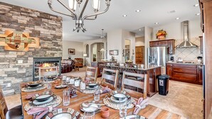 A spacious dining area with a stone fireplace, a chandelier, and a kitchen with modern appliances.