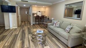 A living room with a sofa, coffee table, and a TV. There is a kitchen area in the background with a dining table and chairs. - Peaceful condo nestled in the heart of Innisbrook (Palm Harbor)