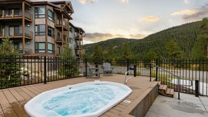 A wooden deck with a hot tub, a fenced area, and a view of a mountain and forest. - 204 Clearwater Lofts 2 Bedroom Condo by RedAwning (Keystone)