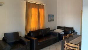 Ein Wohnzimmer mit einer Sofagarnitur, einem Esstisch mit Stühlen und einem Fenster mit Vorhängen.