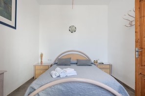 A bedroom with a bed, two bedside tables, a wooden door, and a wall-mounted light fixture.