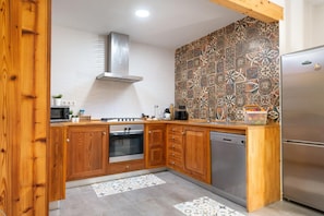 A modern kitchen with wooden cabinets, a stainless steel range hood, a tiled backsplash, and a built-in dishwasher.