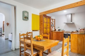 A dining area with a wooden table and chairs, a bowl of fruit, and a yellow window blind.