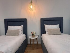 Ett rum med två sängar, var och en med en sänggavel, ett litet runt bord med en korg full av blommor och en hängande lampa.
