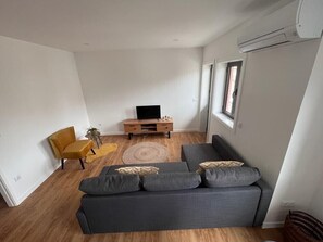 Ett modernt vardagsrum med en grå soffa, en gul fåtölj, ett TV-bord i trä och ett stort fönster.
