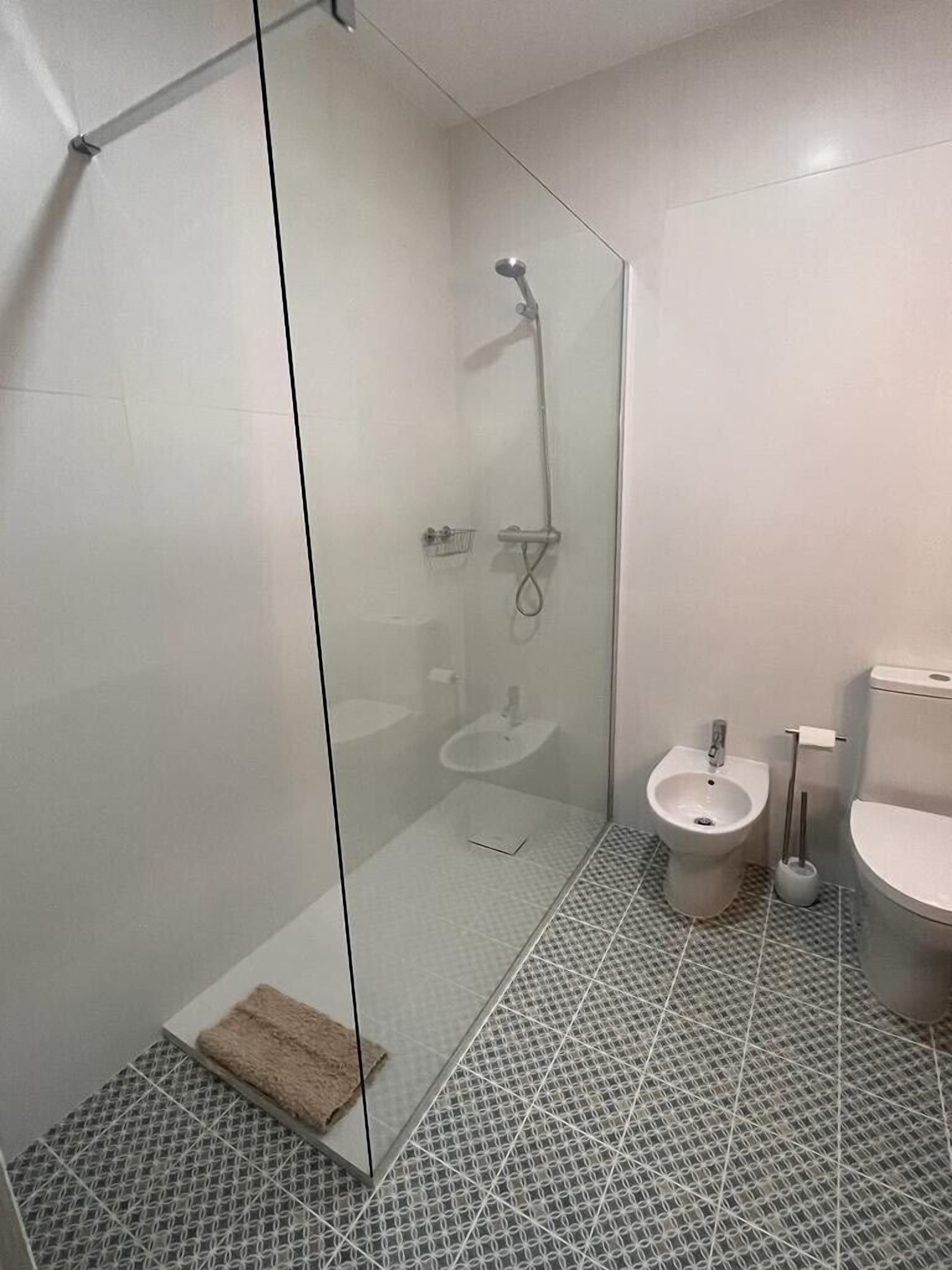 Een moderne badkamer met een douchecabine van glas, een hygiëneschaal en een toilet.
