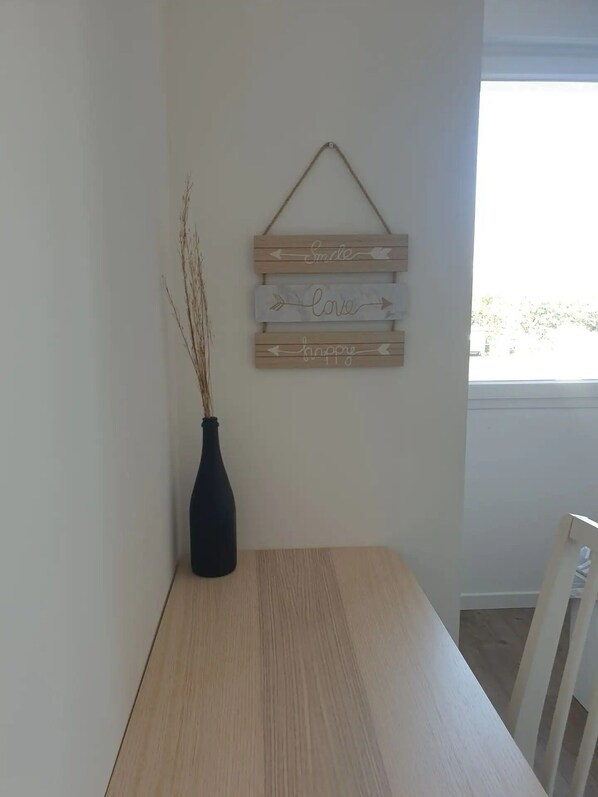 A dining area with a wooden table, a black vase with branches, and a wall-mounted wooden sign with words.
