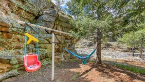 Un hamac tendu entre des rochers et des arbres, une balançoire et une chaise rouge.