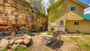 Un mur de pierres apparentes, un banc en bois et une maison jaune avec un toit vert.