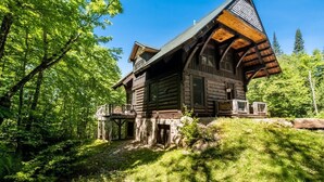 Eine Blockhütte mit steilem Dach, einem Steinfundament und einer Holzterrasse.