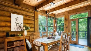 Innenansicht einer Holzhütte mit Esstisch, Stühlen, einer Blumenvase und einem Bild mit einer Eule.