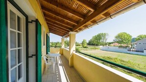 A balcony with a wooden ceiling, white chairs, and a view of a grassy area and buildings in the background. - Sausan Apartments (Corfu)