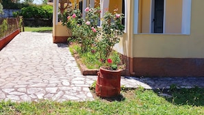 A two-story building with a tiled entrance and a garden with potted plants. - Sausan Apartments (Corfu)