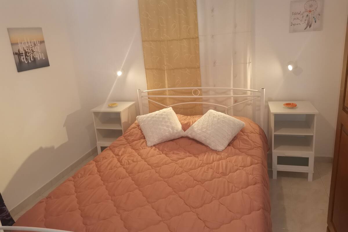 A neatly arranged bedroom with a single bed, two pillows, a nightstand, and a bedside table.