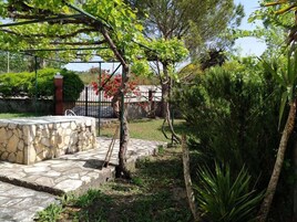 Un patio de piedra con una pequeña mesa, rodeado de abundante follaje y un árbol con flores rojas.