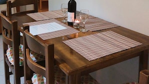 A dining area with a wooden table, chairs, and a bottle of wine. - Sausan Apartments (Corfu)
