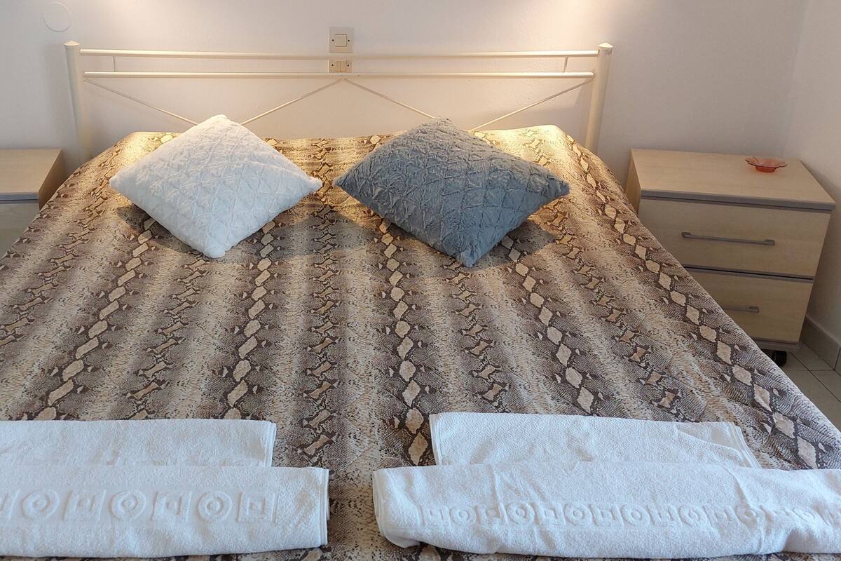 A bed with a patterned bedspread, two pillows, and two folded towels.