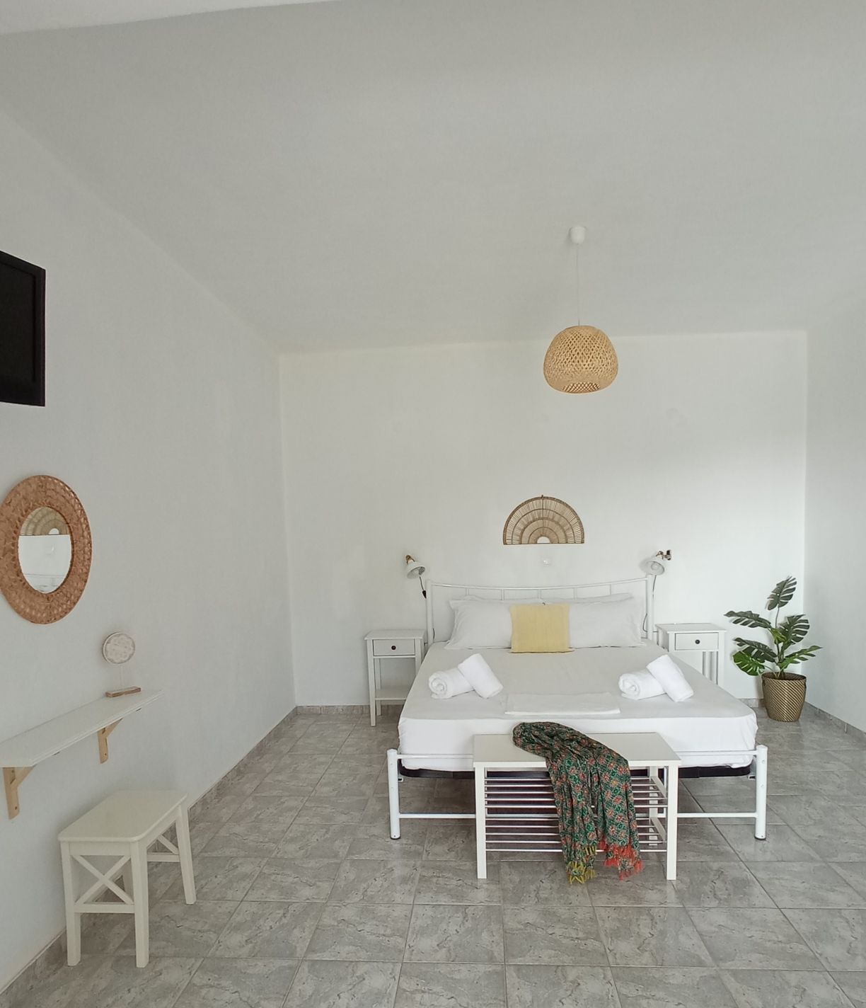 A minimalist bedroom with a single bed, bedside tables, a small stool, and a potted plant.