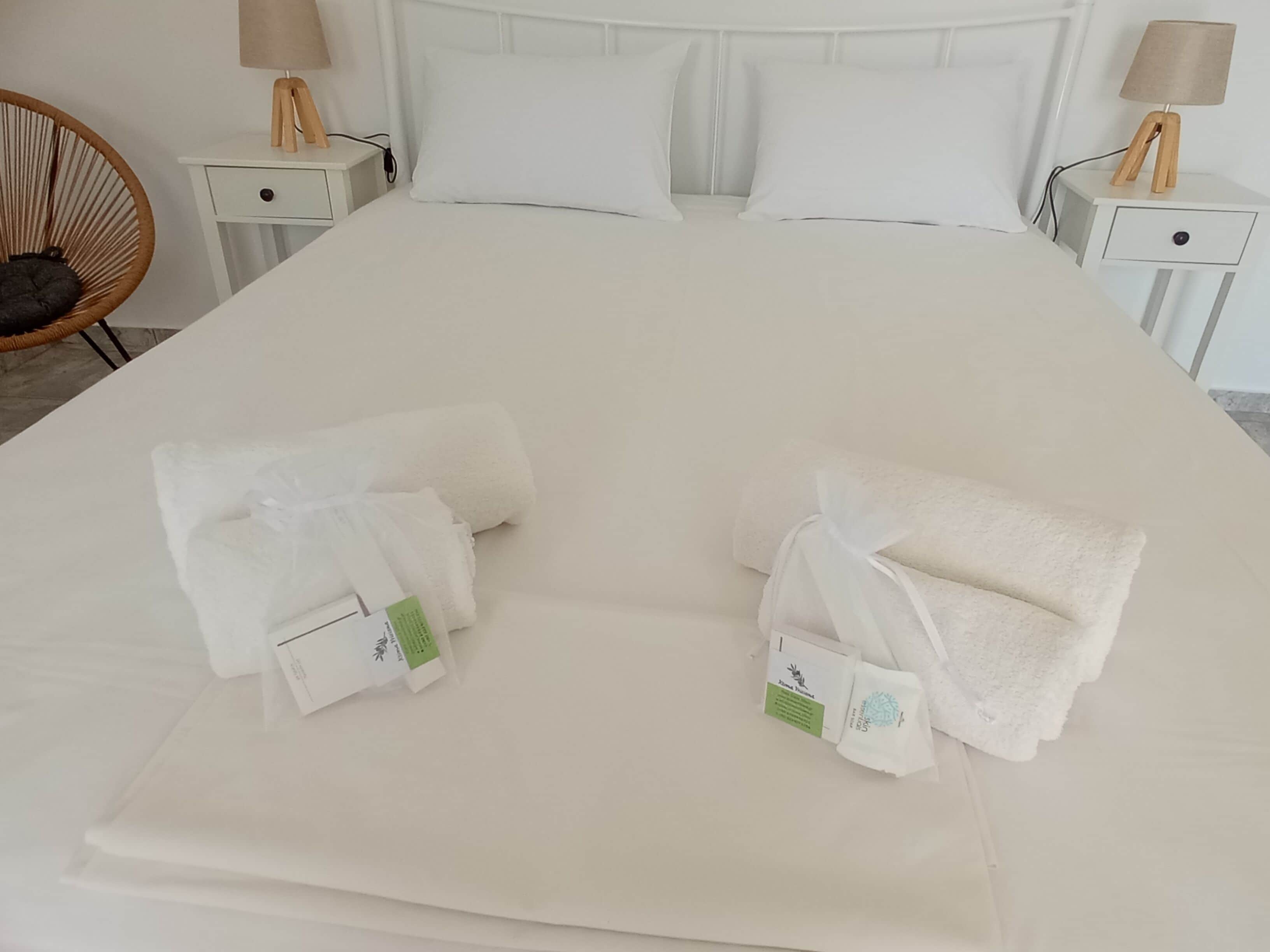 Un letto ben rifatto con lenzuola bianche, due asciugamani piegati con etichette e due comodini con lampade.