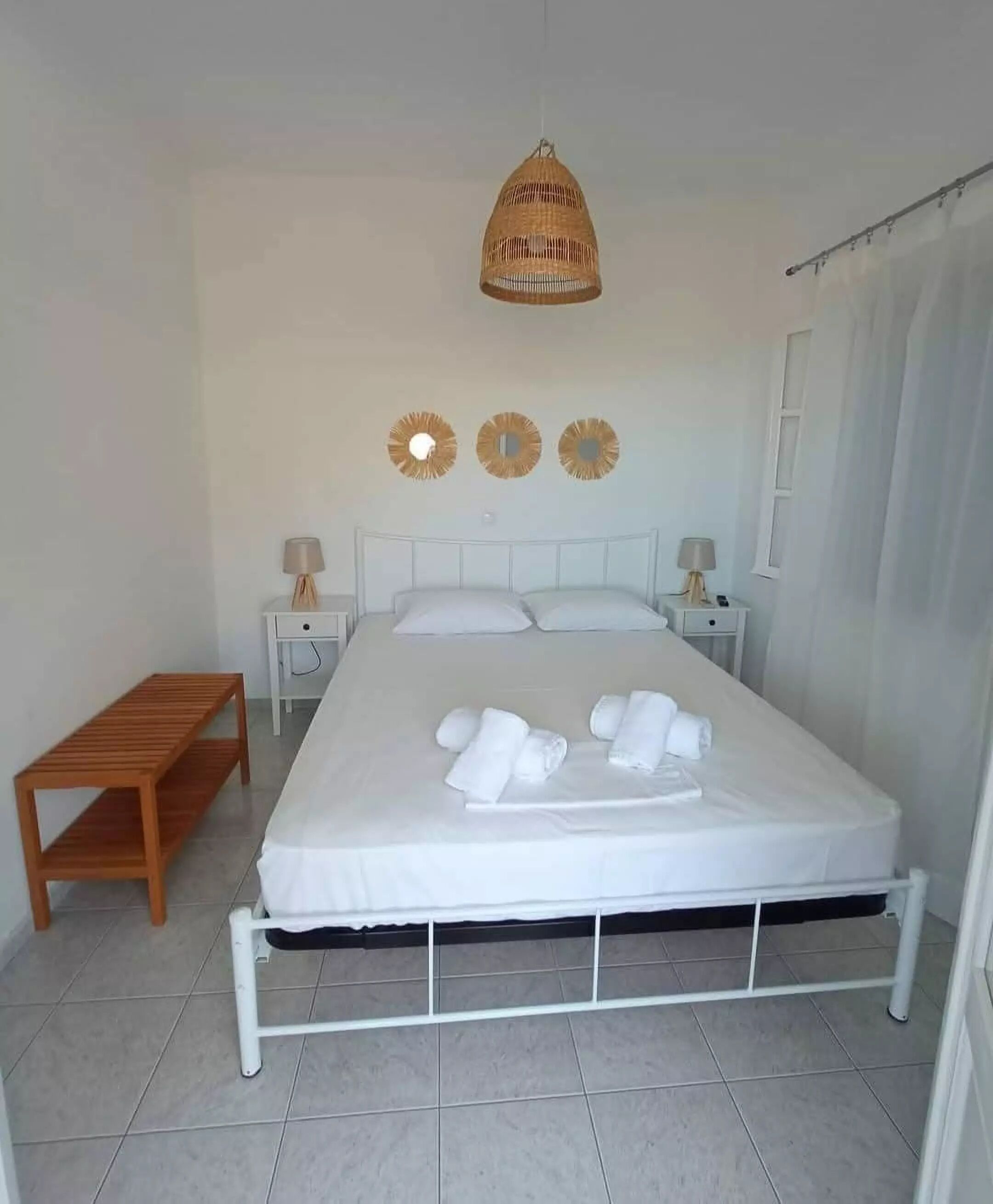 A neatly made bed with white linens and towels, a wooden nightstand with a lamp, and a hanging light fixture above.