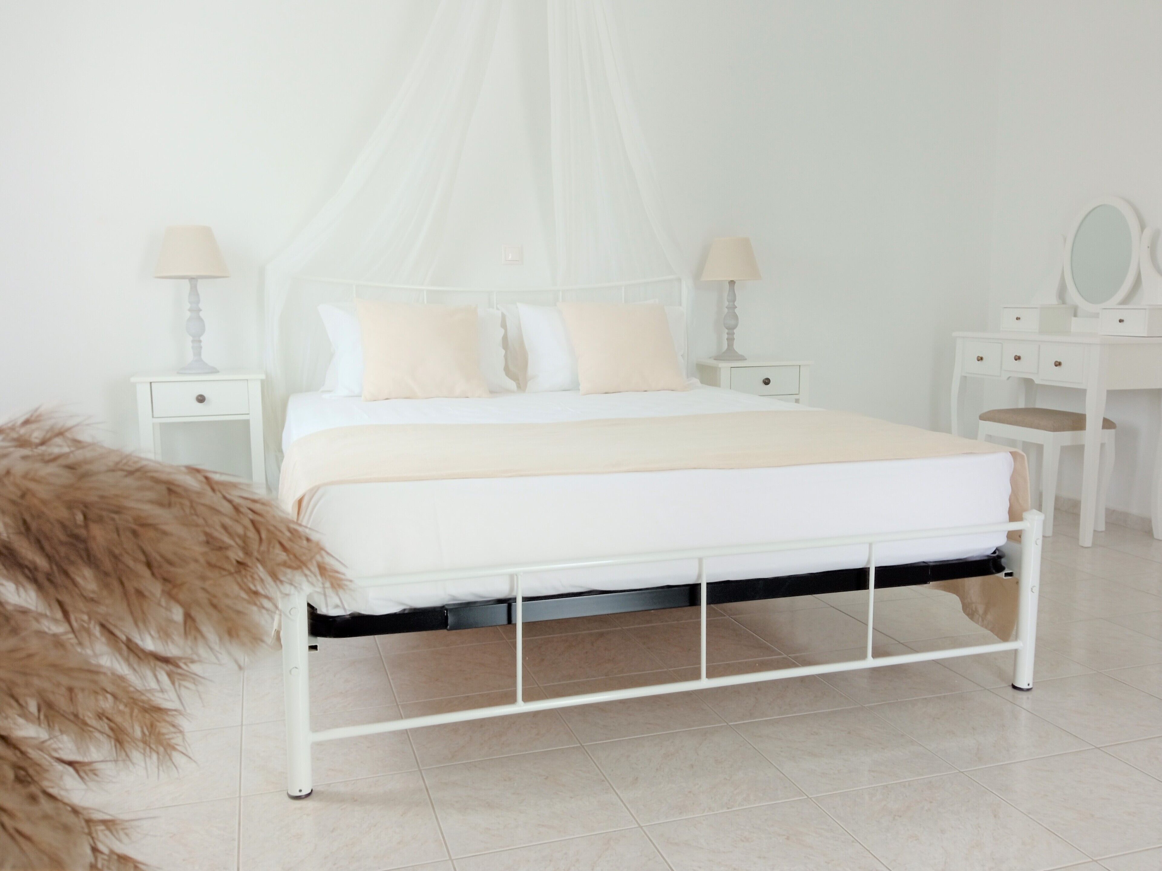 A white four-poster bed with a canopy, two bedside tables with lamps, a dressing table with a mirror, and a fluffy brown object on the floor.