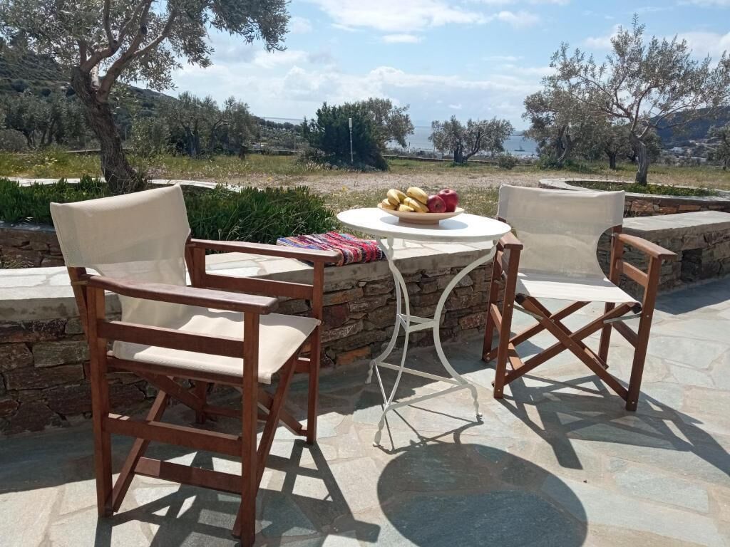 An outdoor seating area with stone walls, two wooden chairs, a round table, and a bowl of fruit.
