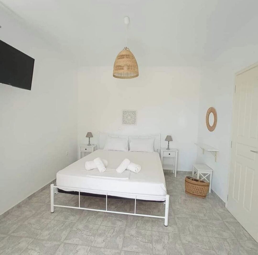 Un dormitorio minimalista con cama blanca, dos mesitas de noche, una lámpara colgante y una puerta.