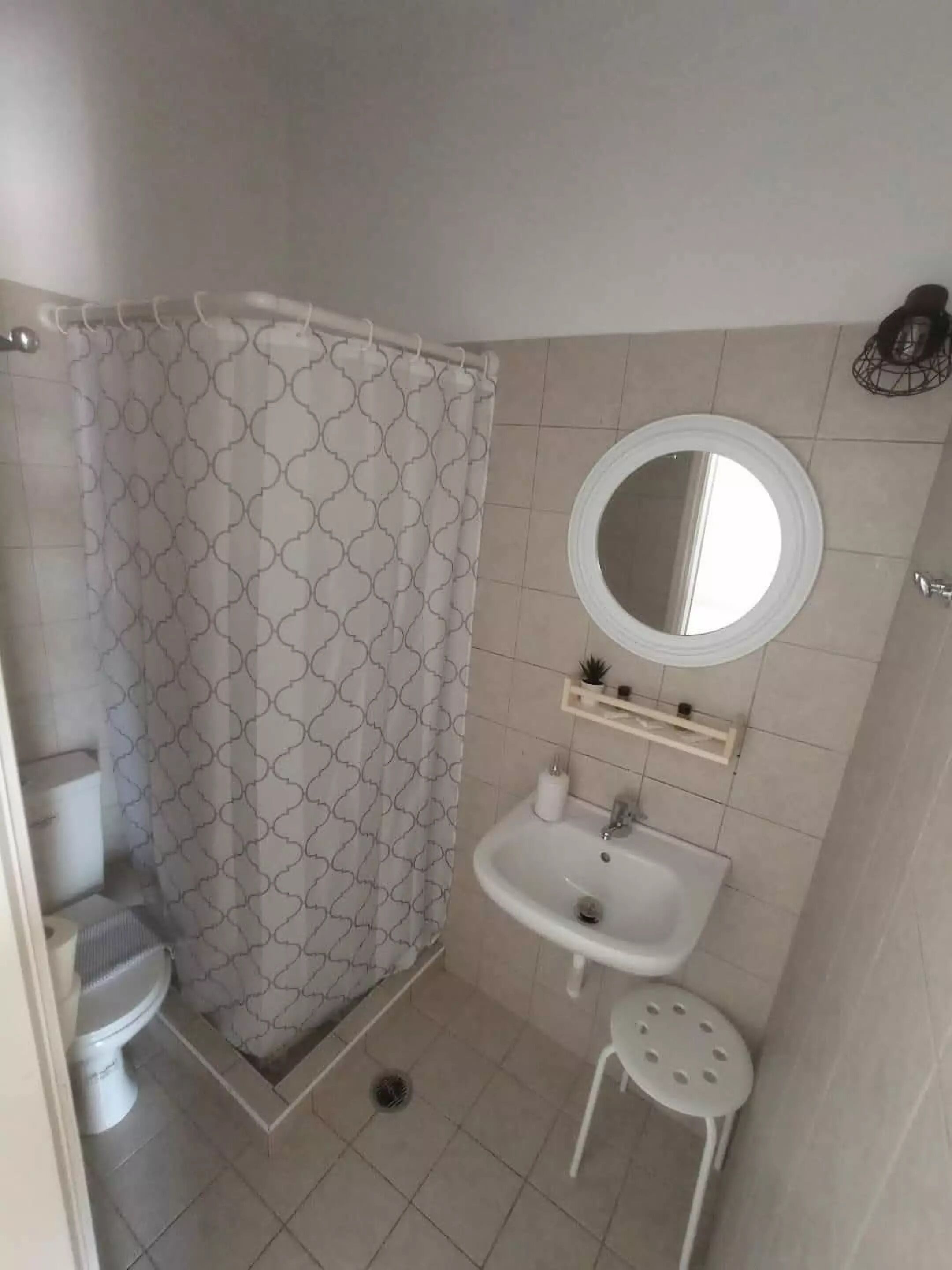 A small bathroom with a shower, toilet, sink, and a mirror.