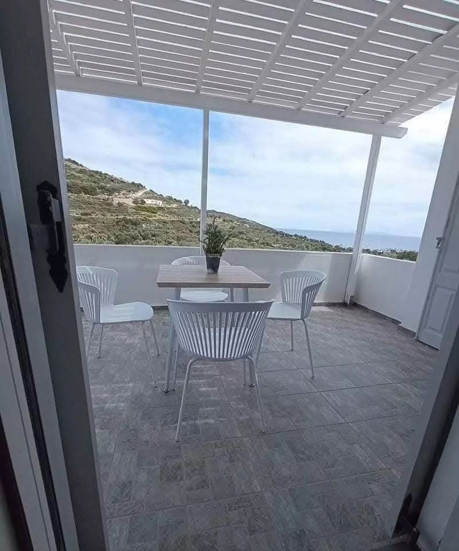 Een terras buiten met een tafel, stoelen, een plant in pot en uitzicht op een heuvellandschap.