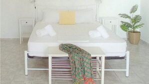 A neatly arranged bedroom with a bed, bedside tables, a hanging light fixture, and a potted plant. - Ktima Vrisiana (Sifnos)