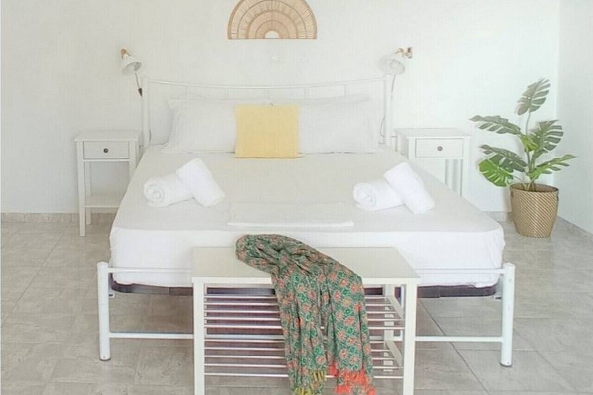 A neatly arranged bedroom with a bed, bedside tables, a hanging light fixture, and a potted plant.