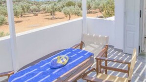 A balcony with a table and chairs, overlooking a coastal landscape with olive trees and a view of the sea. - Ktima Vrisiana (Sifnos)