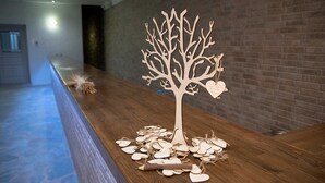 A wooden tree sculpture with heart-shaped leaves and tags on a wooden table in a hallway. - Ktima Vrisiana (Sifnos)