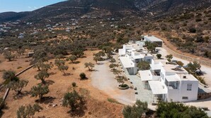 A cluster of white buildings with flat roofs, arranged in a row along a dirt road, surrounded by sparse vegetation and hills in the background. - Ktima Vrisiana (Sifnos)