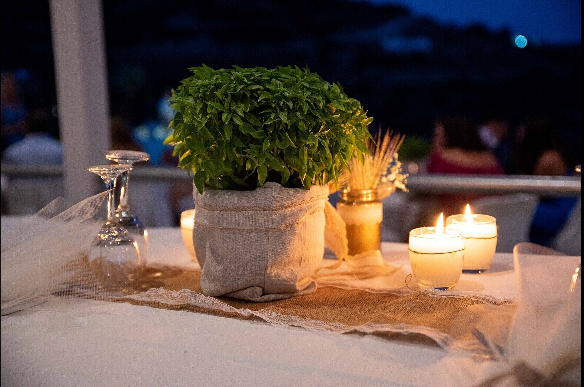A table set with a potted plant, candles, and a glass candle holder.