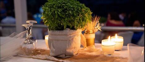 A table set with a potted plant, candles, and a glass candle holder.