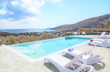 A swimming pool with white lounge chairs and a view of the sea and hills.