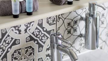 A bathroom with a white sink, two chrome faucets, and a patterned backsplash.
