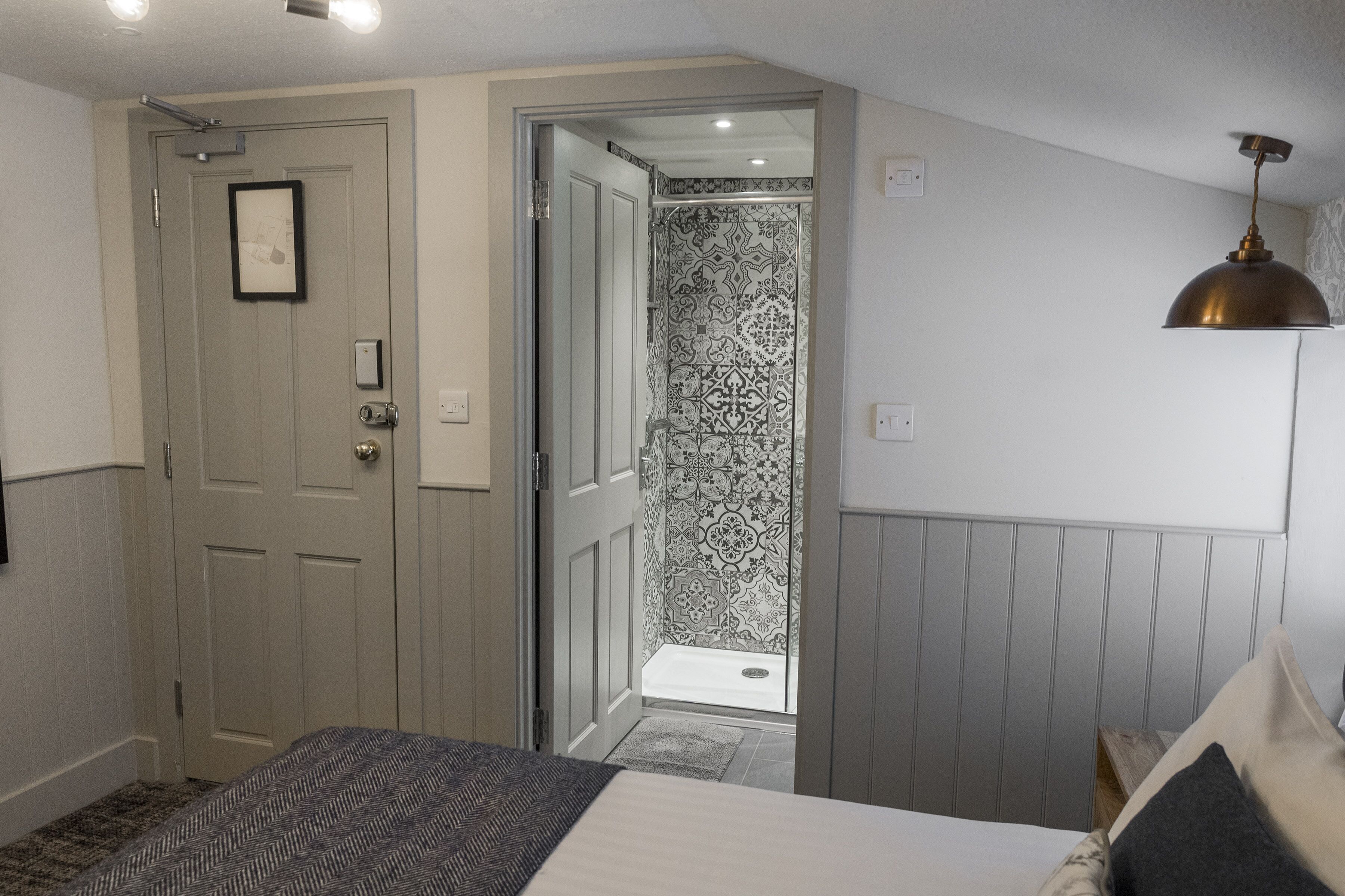 A bedroom with a bed, a door, a shower, and a pendant light.
