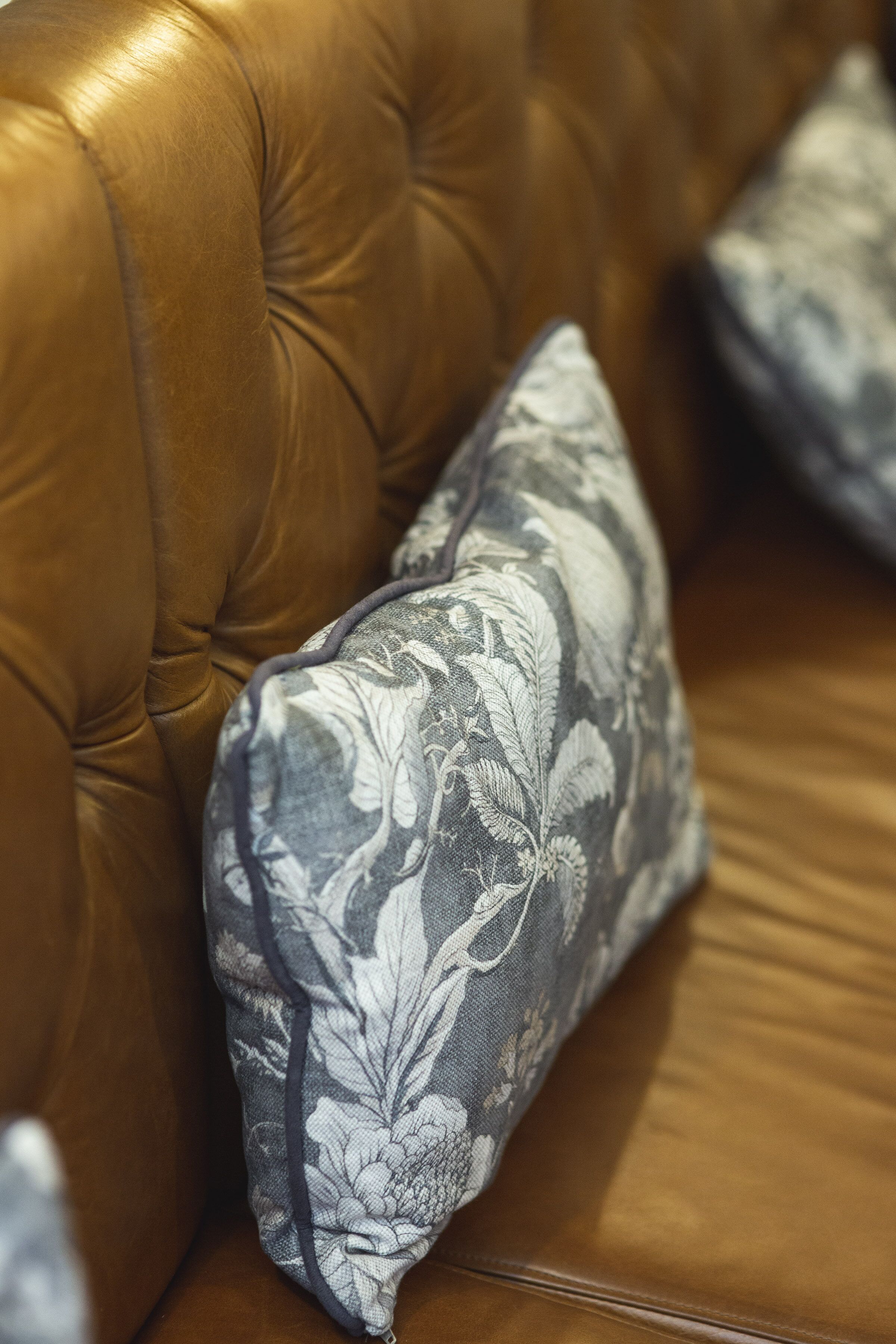 A brown leather sofa with a floral-patterned pillow.