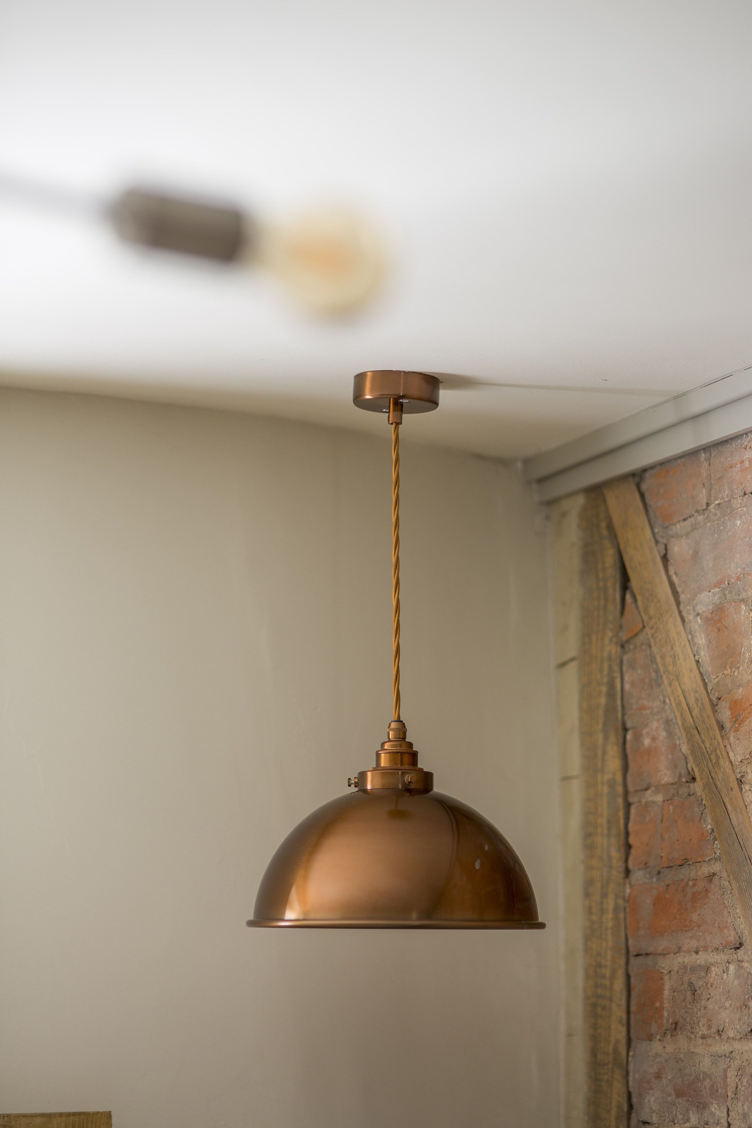 Una lámpara colgante de cobre suspendida del techo en una habitación con pared de ladrillo.