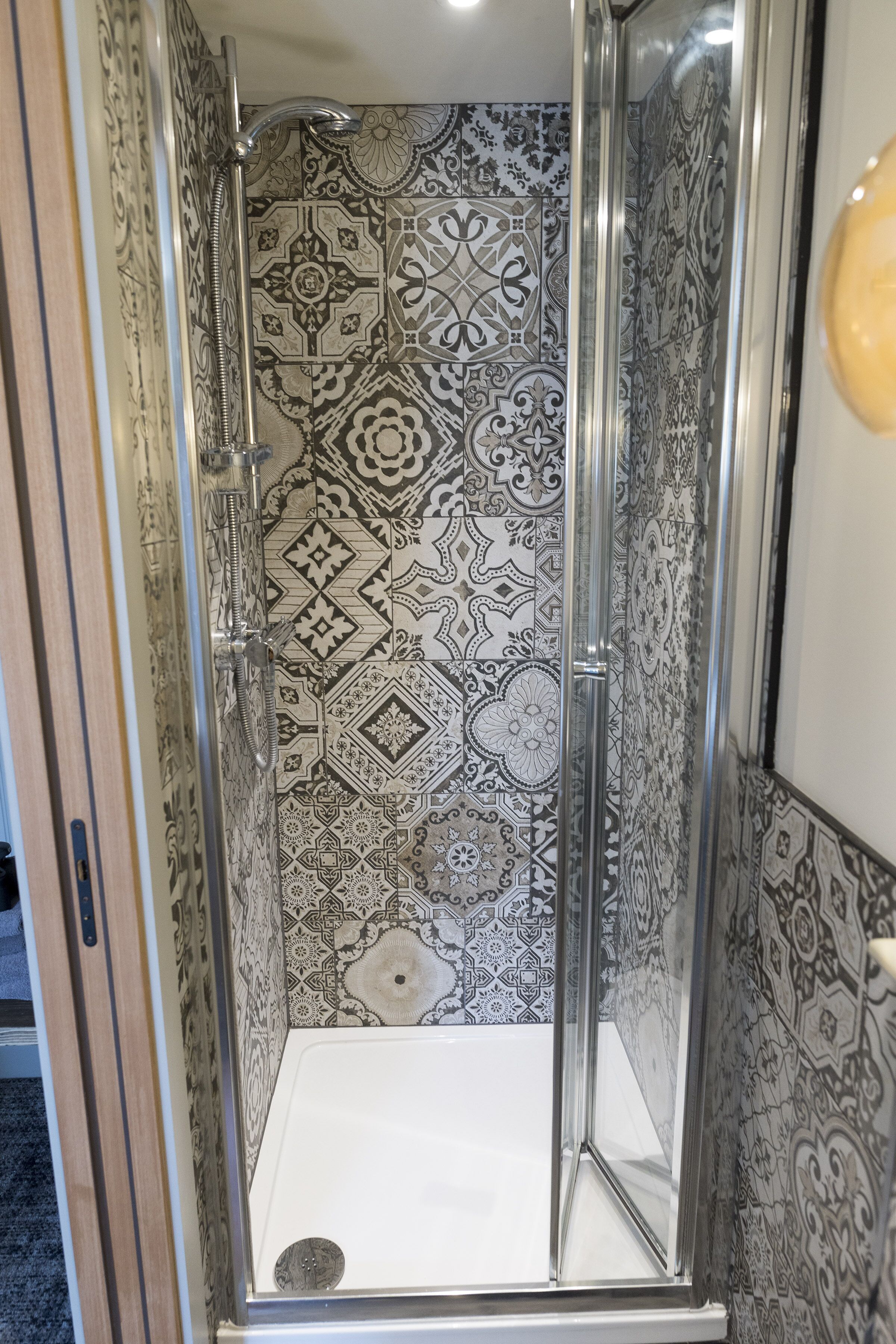 A shower with patterned tiles and a clear glass door.