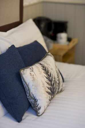 A bed with two pillows, one dark blue and one with a tree pattern, and a wooden nightstand with a coffee maker. - Royal Oak (Dover)