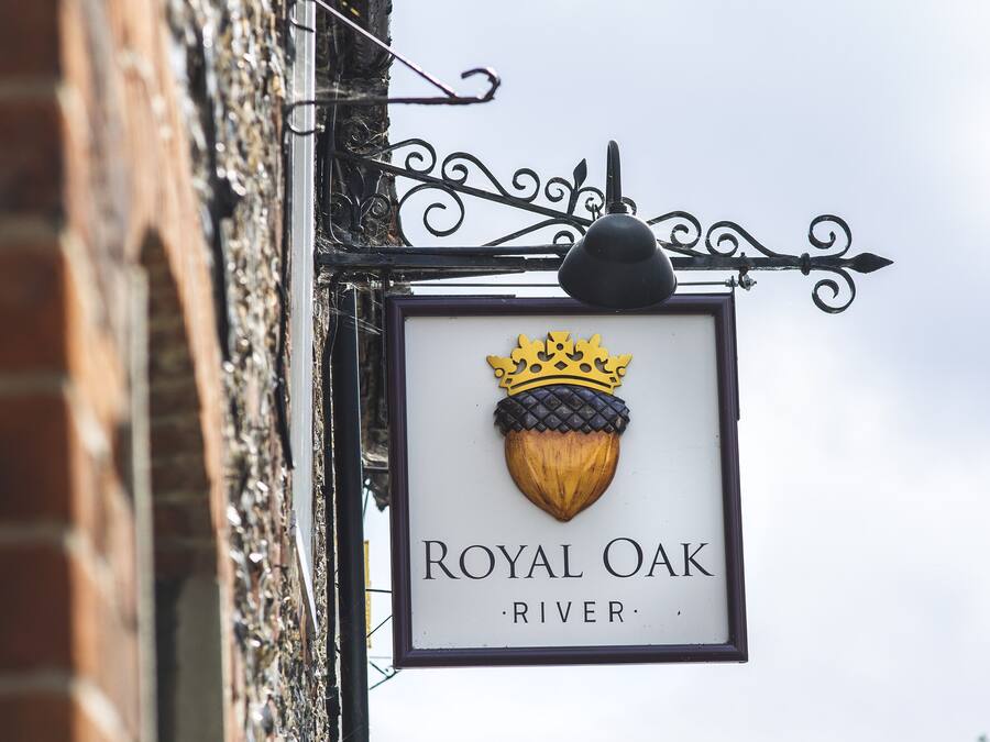 Segnaletica con la scritta 'Royal Oak River' e un emblema con una corona, fissata a un edificio in mattoni con insegna in ferro battuto.