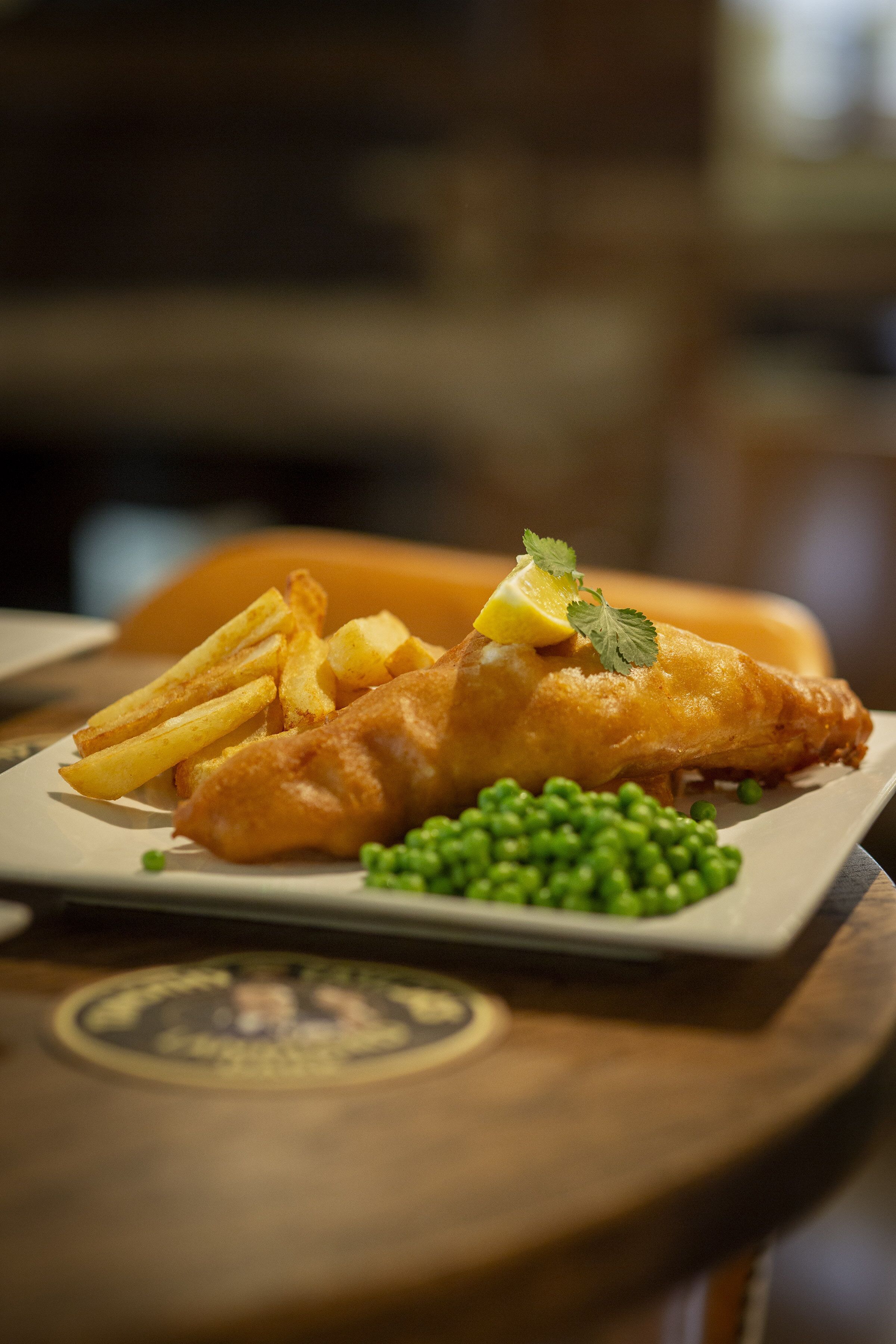 A plate of fish and chips with peas and a lemon wedge on a wooden table.