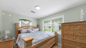 A bedroom with a wooden bed, a nightstand, a dresser, and a window with blinds. - Waterfront Fishing Cottage, 2 King Beds, 75in HDTV, Family Friendly (Jacksonville)