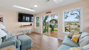 A modern living room with a flat-screen TV, a sofa, and a dining area. - Waterfront Fishing Cottage, 2 King Beds, 75in HDTV, Family Friendly (Jacksonville)