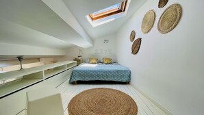 Een slaapkamer met dakraam, een bed met behang, een rond geweven vloerkleed en wanddecoratie van geweven kunst.