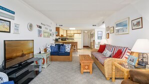 A living room with a TV, sofa, and a dining area with a kitchen in the background.