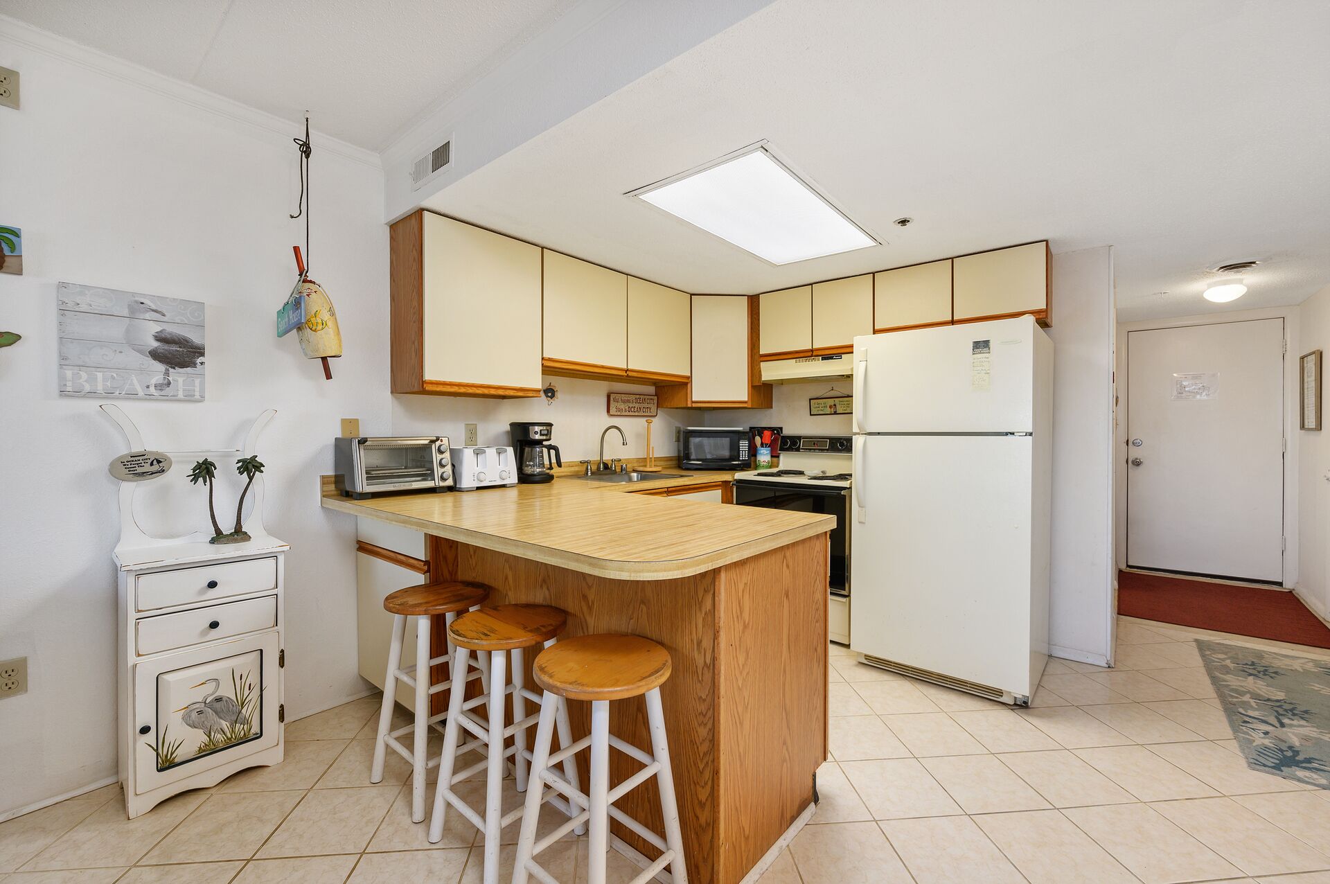 A compact kitchen with a central island, bar stools, a microwave, a toaster, and a refrigerator.
